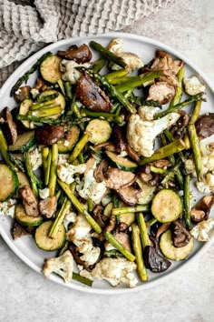 a white plate filled with vegetables and mushrooms on top of a table next to a gray towel