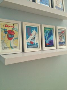 four framed posters are hanging on the wall above a shelf in a room with blue walls