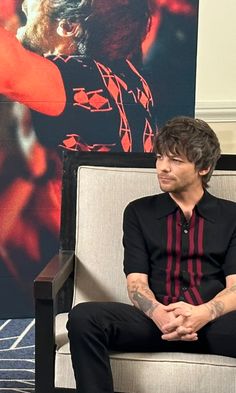 a man sitting in a chair with his hands crossed and looking at something on the wall behind him