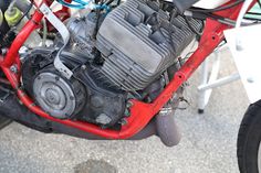 the engine of a red motorcycle parked in a parking lot next to other motorcycles and bicycles