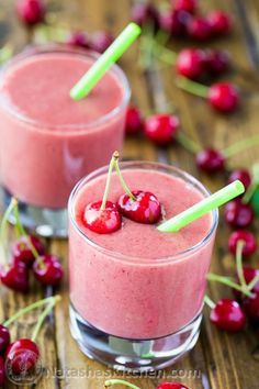 two glasses filled with smoothie and cherries on a wooden table next to fresh cherries