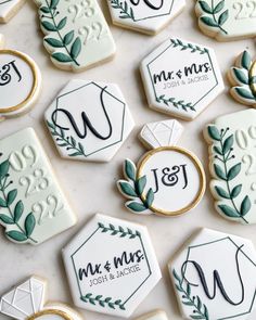 wedding cookies decorated with green leaves and monogrammings are displayed on a table