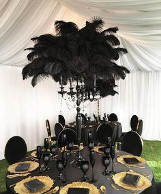 the table is set up with black and gold place settings, silverware, and an ostrich feather centerpiece