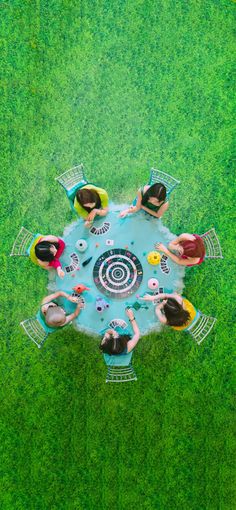 four people sitting at a table in the middle of a green field, top view from above