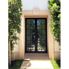 an entrance to a house with glass doors and trees in the front yard, on a sunny day