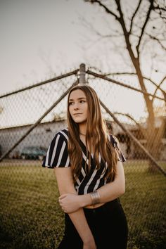 a woman standing in front of a fence with her arms crossed and looking at the camera