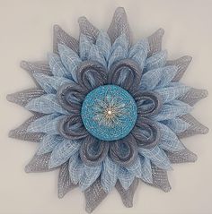 a blue and gray flower on a white wall with some feathers around the center that is shaped like a sunflower