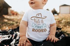 a baby sitting on top of a blanket wearing a cowboy hat and first rodeo shirt