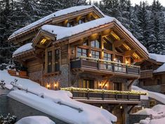 a large wooden house covered in snow with lights on the balconies and windows