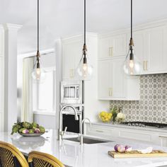 three lights hanging over a kitchen island in a white kitchen with marble counter tops and yellow chairs