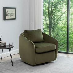 a living room with a chair, table and large glass window looking out onto the woods