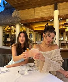 two women sitting at a table with drinks in their hands and one holding a drink