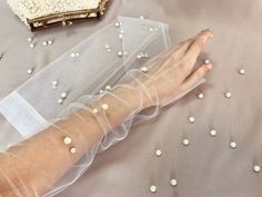 White Pearl Fingerless Gloves, the perfect accessory for elegant evenings and unforgettable wedding moments. These gloves are designed to add a touch of glamour and sophistication to your attire, with their stunning pearl decorations and fingerless style.The White Pearl Fingerless Gloves are a true embodiment of elegance and grace. Crafted with meticulous attention to detail, they feature delicate white tulle fabric that gracefully drapes over the hands, leaving the fingers free for movement and Elegant Fingerless Bridal Accessories For Wedding, Elegant Fingerless Bridal Accessories For Party, White Tulle Fabric, Gloves Style, Pearl Decorations, Gloves Design, Bridal Gloves, White Tulle, Wedding Moments