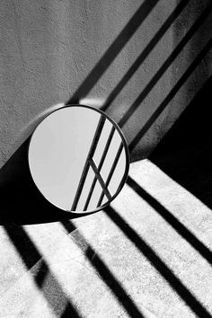 a round mirror sitting on the side of a wall next to a shadow filled wall