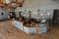 a large room with wood flooring and stone wall decor on the walls, along with two people sitting at a bar