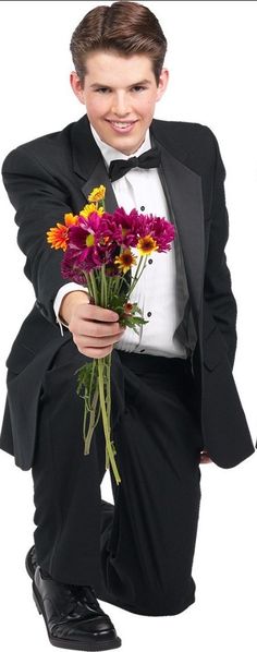 a young man in a tuxedo holding flowers