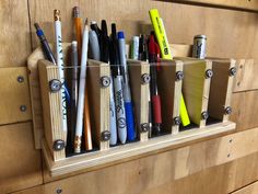 several pens and pencils are in a holder on a wooden wall with drawers behind them