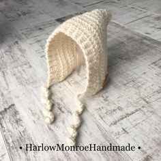 a white crocheted hat sitting on top of a wooden floor next to a wall