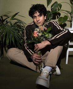 a man sitting on the ground with flowers in his hand and wearing adidas sneakers