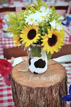 a vase filled with sunflowers sitting on top of a wooden table next to a red and white checkered table cloth