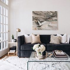 a living room filled with furniture and a painting on the wall above it's glass coffee table