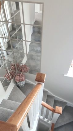 a mirror on the wall next to a stair case and vase with flowers in it