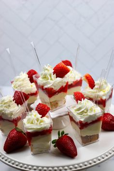 small desserts with strawberries and whipped cream are arranged on a white platter