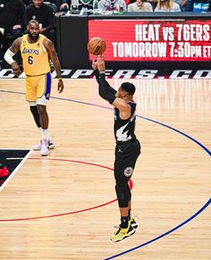 the basketball player is trying to block the ball from going into the basket while another player looks on