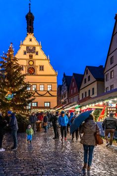 many people are walking down the cobblestone street in front of christmas trees and buildings