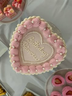 a pink heart shaped cake sitting on top of a table next to other desserts