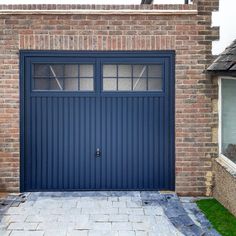 a blue garage door in front of a brick building with grass growing on the ground