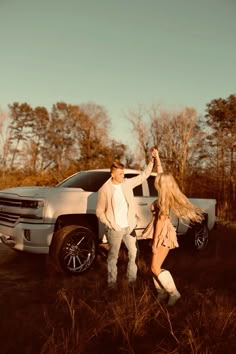 a man and woman standing in front of a white truck with long blonde hair on it