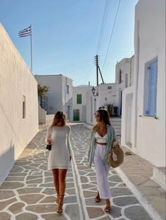 two women walking down a cobblestone street with white buildings and blue shutters