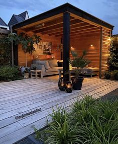 a wooden deck with potted plants and lights on it in front of a house