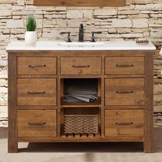 a bathroom vanity with two sinks and a basket under the sink, in front of a brick wall