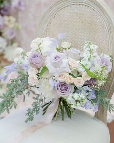 a bouquet of white and purple flowers sitting on top of a chair with greenery