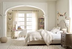 a white bedroom with arched doorway leading to another room that has a bed and desk in it