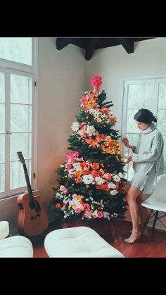 a woman sitting on a chair next to a christmas tree with flowers in the corner