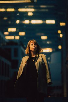 a woman is walking down the street at night with her coat over her shoulders and head tilted to the side