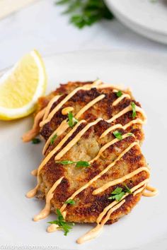 two crab cakes on a white plate with lemon wedges and drizzled sauce