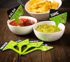 three bowls filled with guacamole, salsa and chips on top of a wooden table