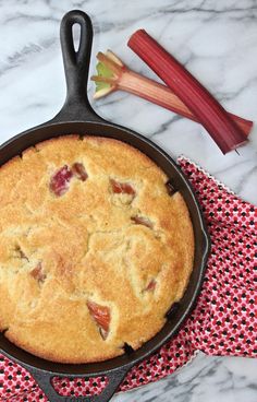 a cast iron skillet with a pie in it and rhubarb stalks next to it