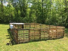 a fenced in sheep pen with trees in the back ground and grass around it