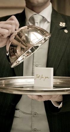 a man in a suit is holding a tray with silver items on it and a card