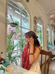 a woman sitting at a table talking on her cell phone while looking out the window