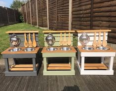 three different colored wooden kitchen sinks with spoons and utensils on them in front of a fence