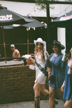 two women in cowboy hats and dresses are walking down the street while one woman is holding a drink