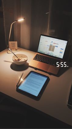 a table with a laptop, tablet and bowl of cereal on it next to a lamp