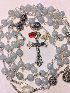 I made this rosary using a very light Aquamarine Gemstone bead,  the color was so soothing to me and relaxed me during the making of this piece.  I used 6mm beads and capped them with small silver caps, for the Pater beads I used an 8mm silver filigree bead with a row of rhinestones through the middle of each bead.  I wire wrapped this rosary with silver plated wire for added strength and durability.  I make my own spacers to separate the decades and for this rosary I used a 3mm light blue AB Austrian crystal bicone bead and added a 2mm sterling silver bead at each end. The Crucifix, centerpiece and medal are hand-cast in solid sterling silver, reproductions of vintage pieces from years ago.  This is a wonderful idea someone had, to preserve and share the amazing designs and workmanship of Silver Hand-strung Rosary As Gift, Silver Rosary With Natural Stones As A Gift, Silver Rosary With Natural Stones For Gift, Handmade Silver Rosary For Healing, Praying The Rosary, Silver Caps, Beaded Skull, Teardrop Beads, Aquamarine Gemstone