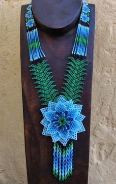 a necklace with blue and green beads on a wooden stand next to a tan wall